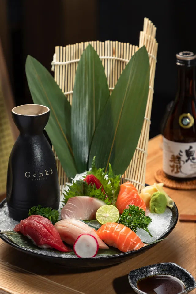 A sashimi platter with leaves, ice and a sake bottle