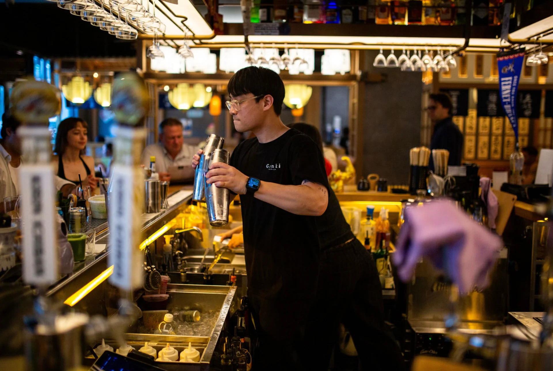 A Genki bartender shakes a cocktail behind the warmly lit bar