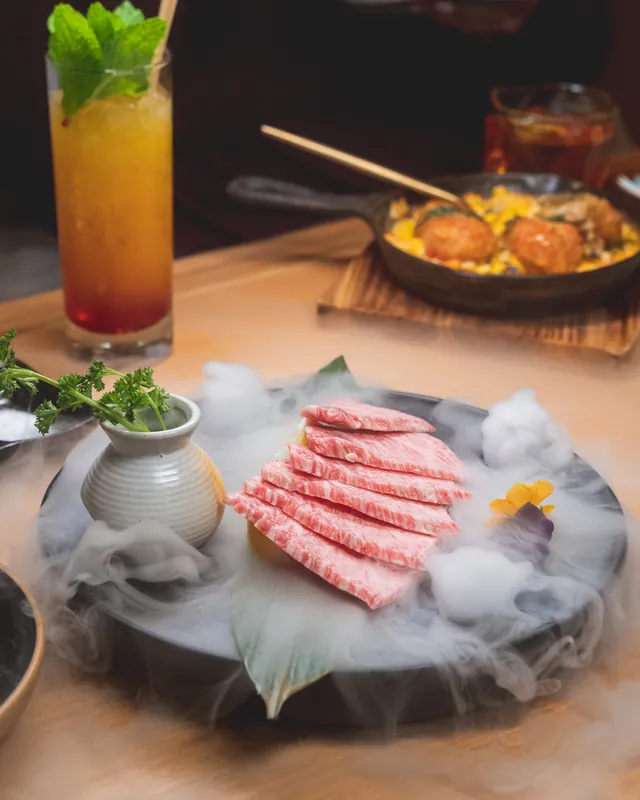 Fanned slices of A5 wagyu on a dark platter swirling with dry-ice smoke